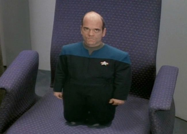 The Doctor from Star Trek: Voyager, shrunk to a few inches tall, standing on an armchair