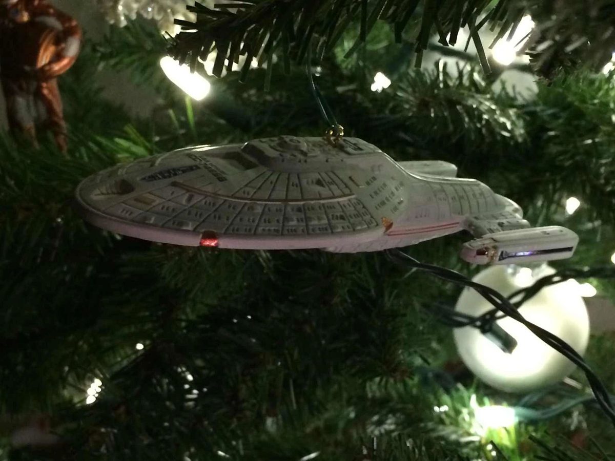A miniature USS Voyager starship ornament hanging on a Christmas tree