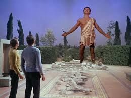 Star Trek still of the god Apollo towering over two Enterprise crewmen in a temple garden