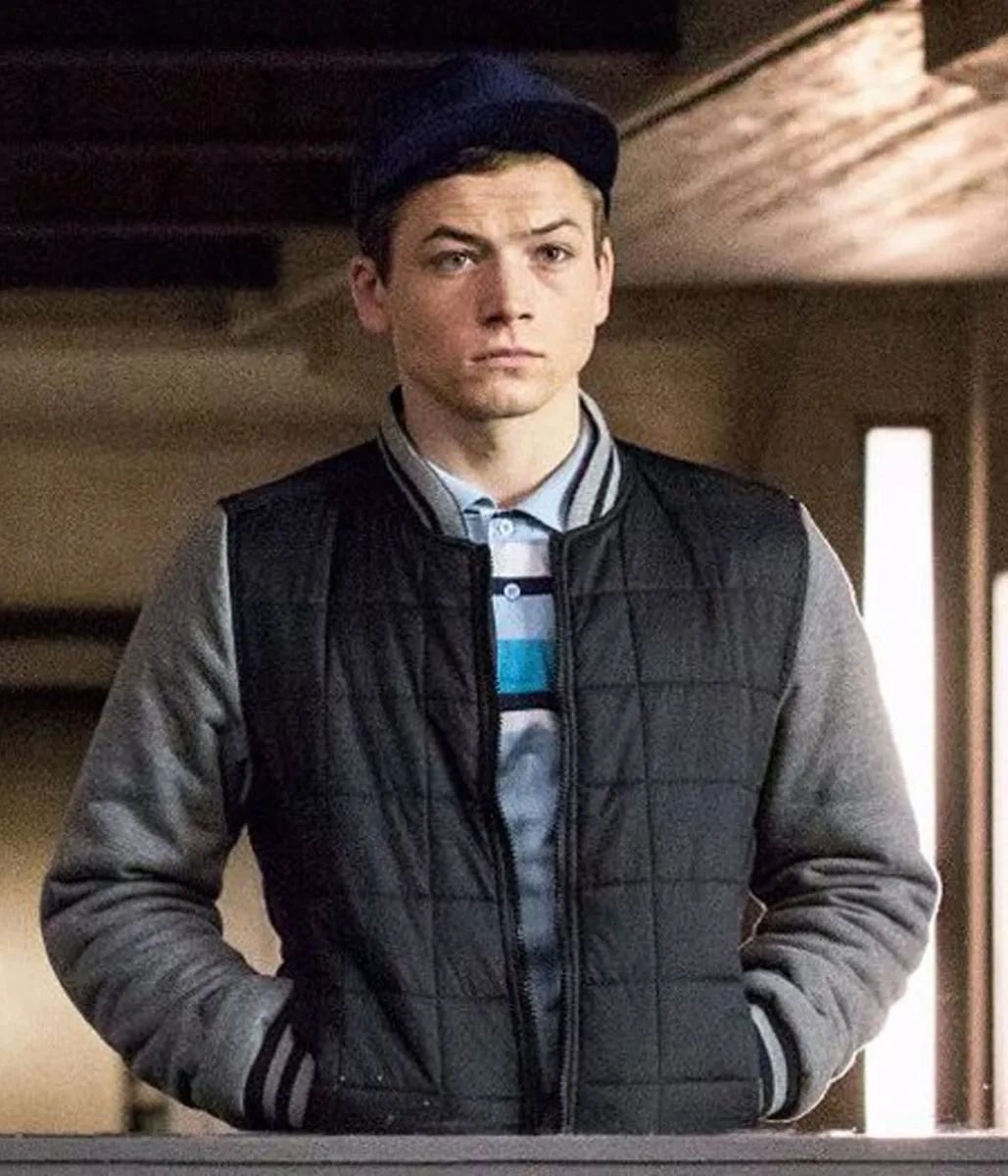 Still of the Kingsman character Eggsy in a cap and padded gilet