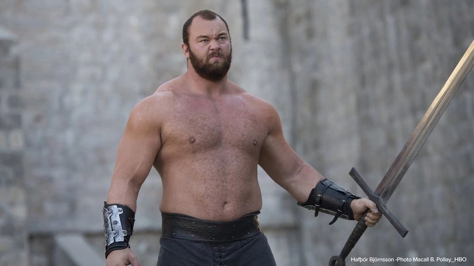 A shirtless, bearded strongman holding a sword