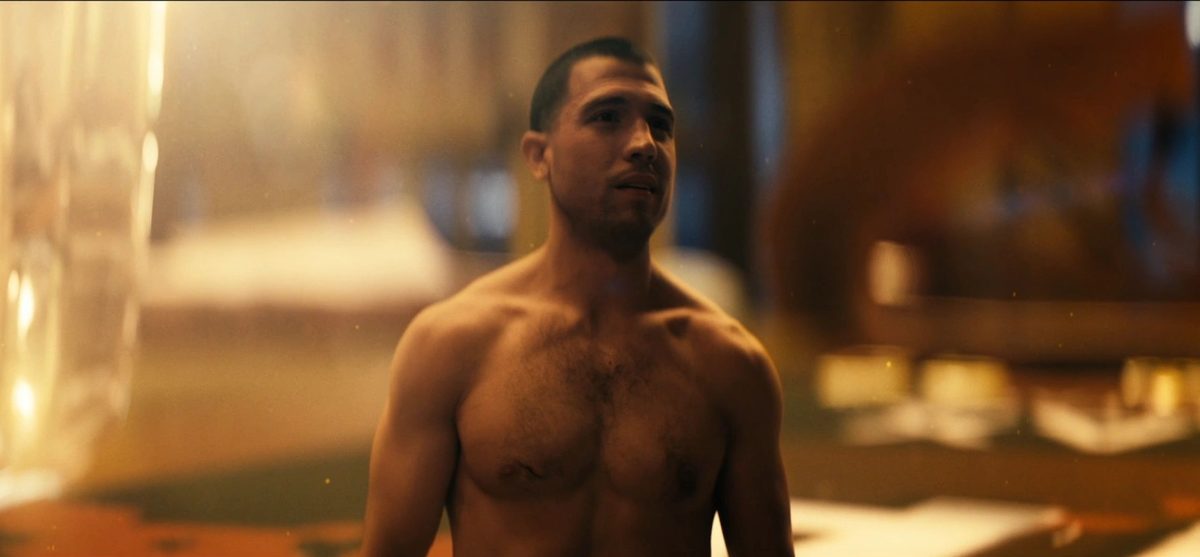 TV still of a shirtless man standing in a warmly lit room