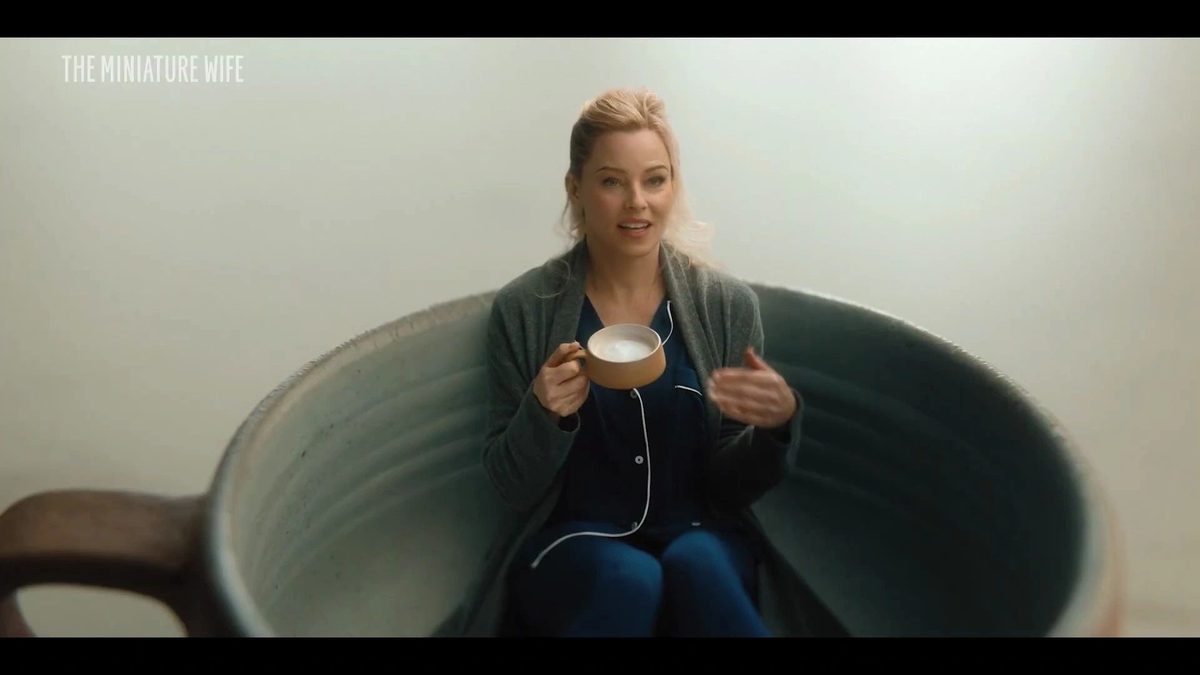 A tiny woman sitting inside a giant teacup holding a spoon